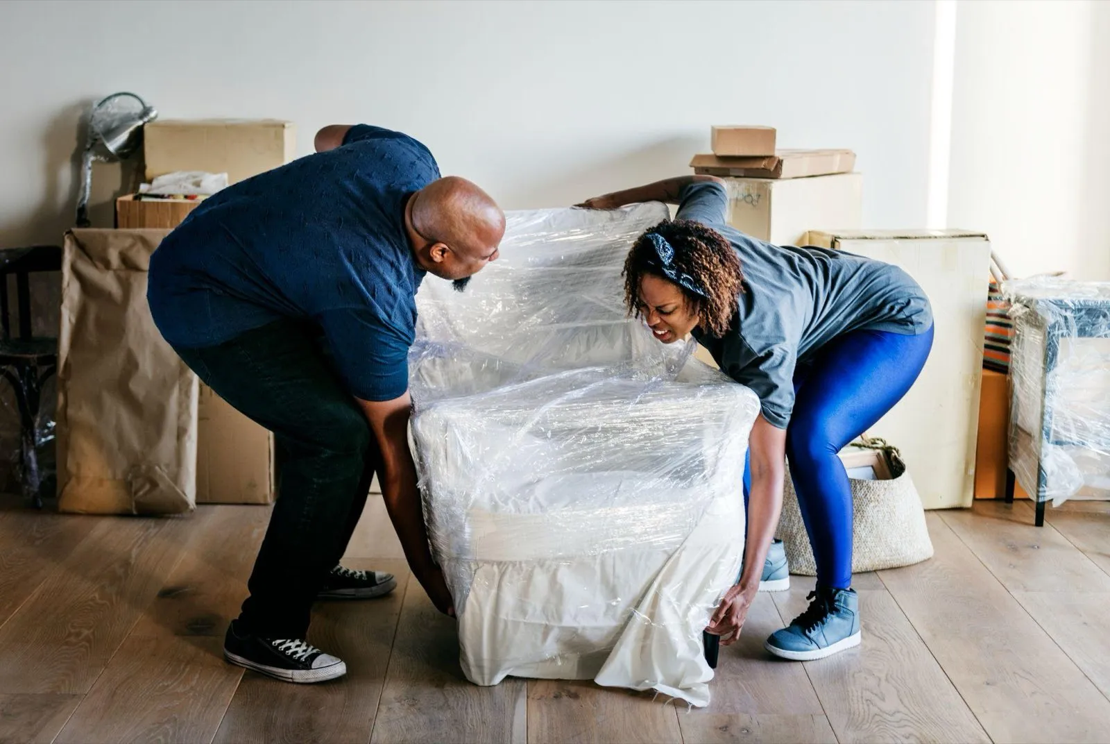 Two people wrapping an armchair in protective plastic before putting it into storage