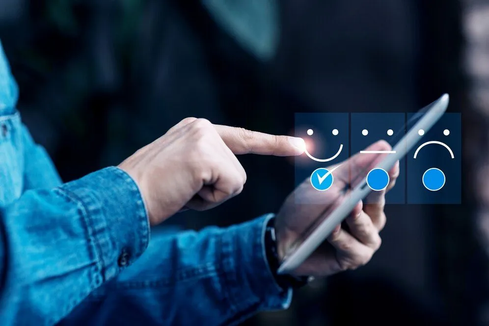 A finger selecting a smiling face on a tablet showing satisfaction ratings