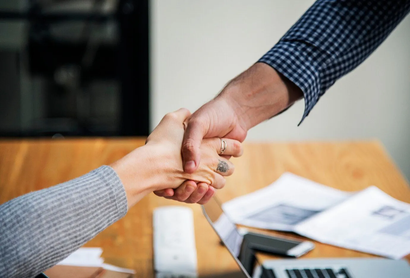 Two people shaking hands across a desk covered in paperwork