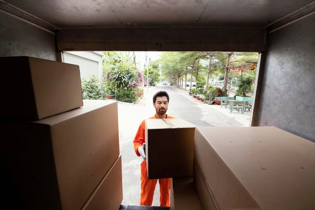 A man carrying a cardboard box into a storage unit stacked with boxes