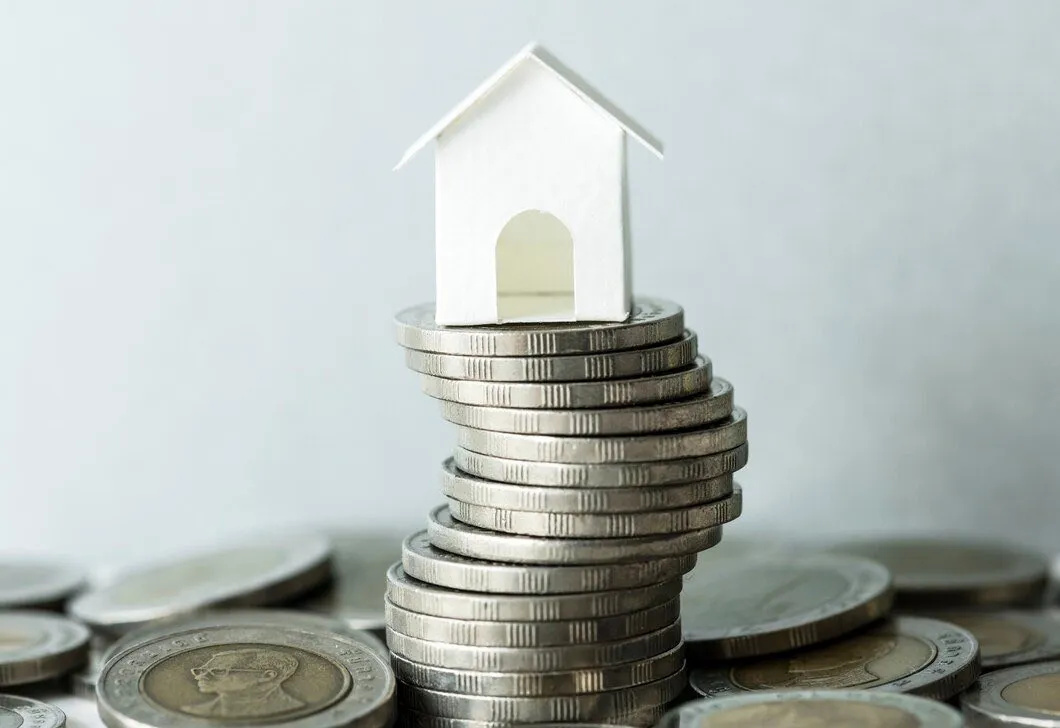 A small model house balanced on a rising stack of coins